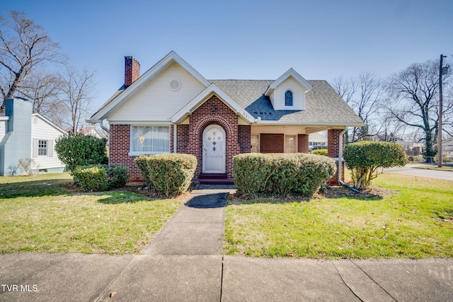 view of front of home with brick siding, a chimney, a front lawn, and a shingled roof