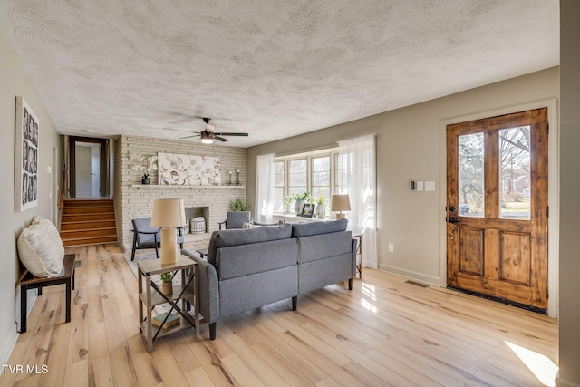 living room with light wood-style flooring, a brick fireplace, a healthy amount of sunlight, and visible vents