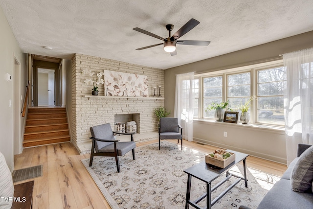 living area with ceiling fan, a textured ceiling, wood finished floors, baseboards, and stairs