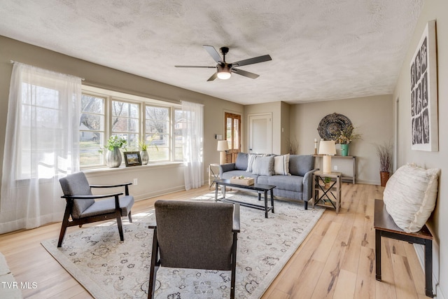 living room featuring a ceiling fan, baseboards, light wood-style flooring, and a textured ceiling