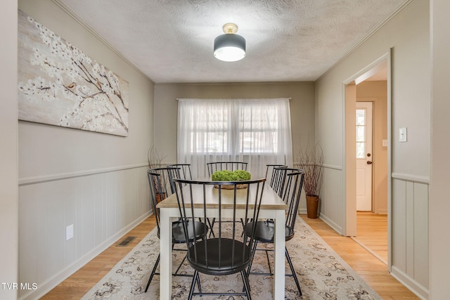 dining space with a textured ceiling, visible vents, light wood-style floors, wainscoting, and crown molding