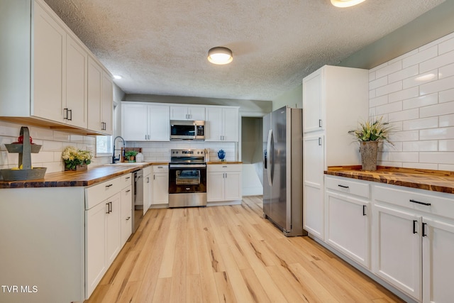 kitchen featuring wood counters, stainless steel appliances, light wood-type flooring, white cabinetry, and a sink