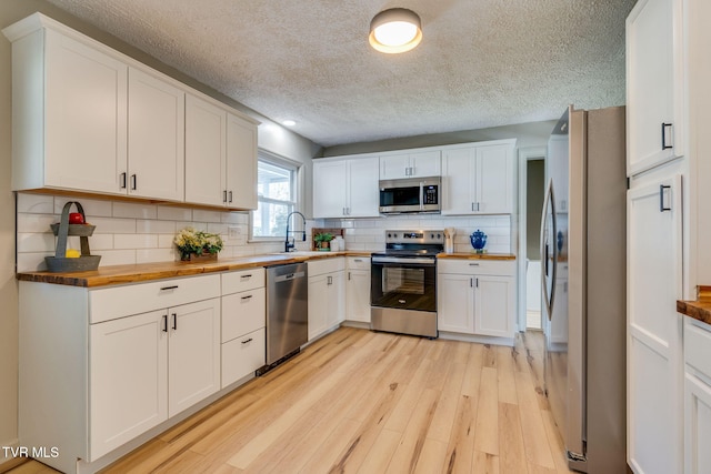 kitchen featuring a sink, wood counters, light wood-style floors, appliances with stainless steel finishes, and tasteful backsplash