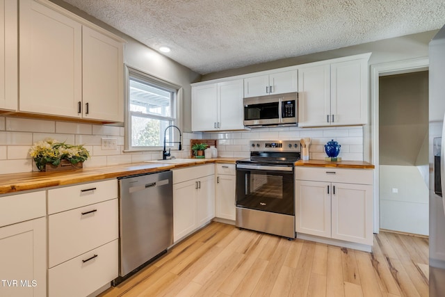 kitchen with white cabinets, butcher block counters, stainless steel appliances, light wood-type flooring, and a sink