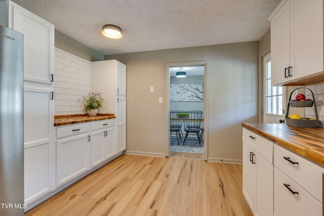 kitchen featuring light wood finished floors, butcher block counters, backsplash, and white cabinets