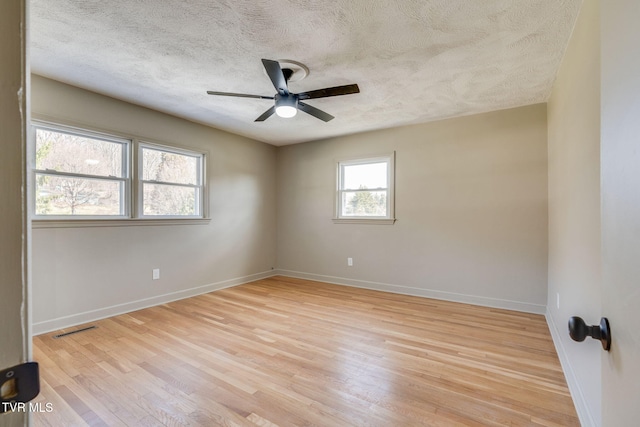 empty room featuring a textured ceiling, ceiling fan, visible vents, baseboards, and light wood finished floors