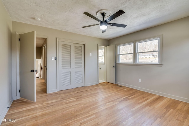 unfurnished bedroom with a closet, baseboards, a textured ceiling, and light wood finished floors