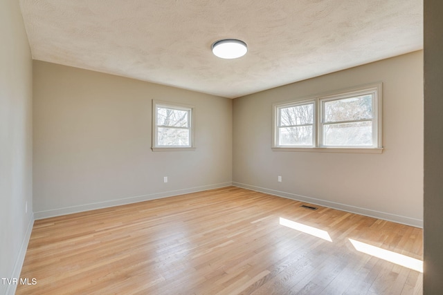 empty room featuring a textured ceiling, light wood-style flooring, visible vents, and baseboards