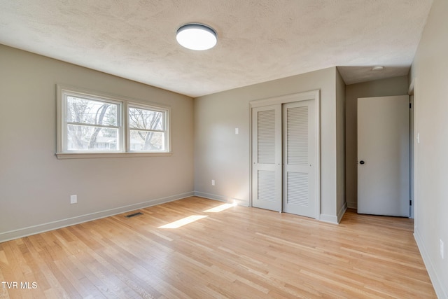 unfurnished bedroom featuring a textured ceiling, light wood-style flooring, visible vents, baseboards, and a closet