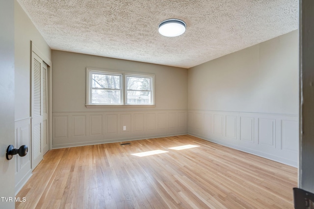 unfurnished room featuring a wainscoted wall, light wood-style flooring, and a textured ceiling