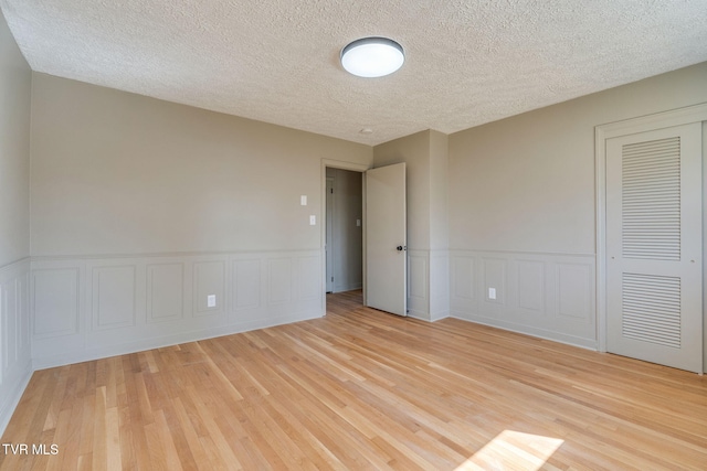 empty room with light wood-style floors, wainscoting, and a textured ceiling