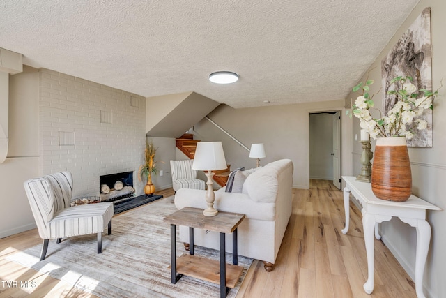 living room featuring light wood-style floors, a brick fireplace, a textured ceiling, and baseboards