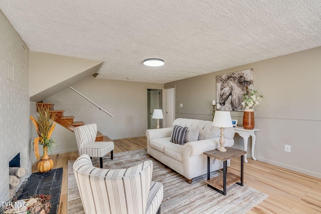 living area featuring baseboards, stairway, wood finished floors, a textured ceiling, and a fireplace