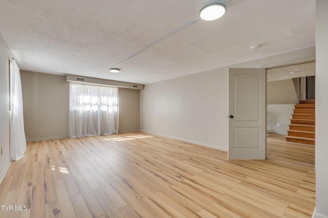 unfurnished room with stairs, a textured ceiling, wood finished floors, and baseboards