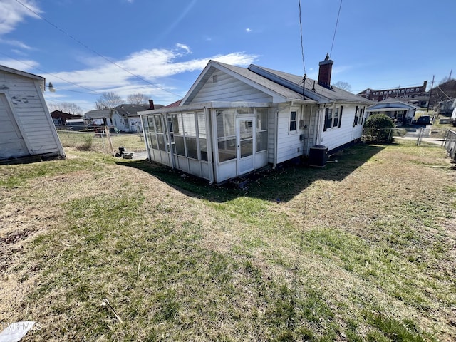 back of property with a sunroom, a lawn, a chimney, and fence