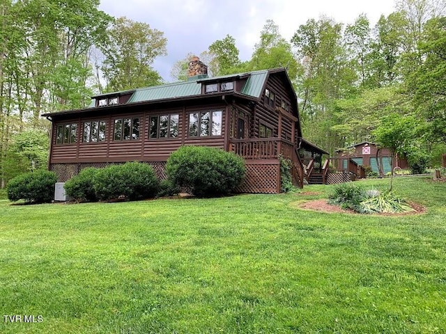 view of side of property with log siding, a lawn, a gambrel roof, and a chimney