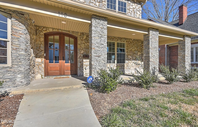 property entrance featuring covered porch, stone siding, and french doors