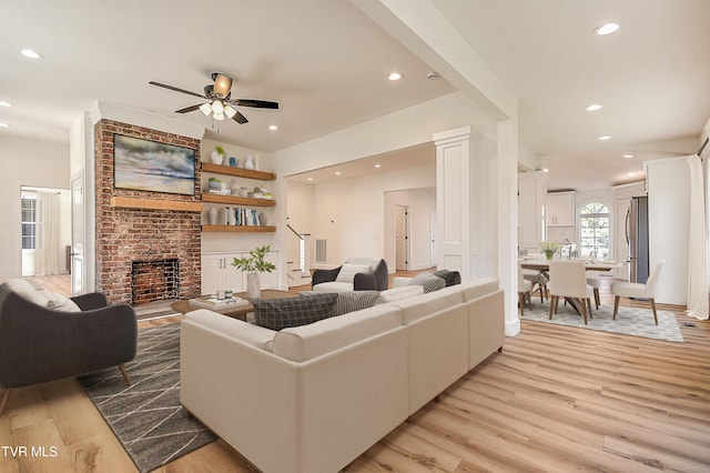 living area with stairs, recessed lighting, a brick fireplace, and light wood-type flooring
