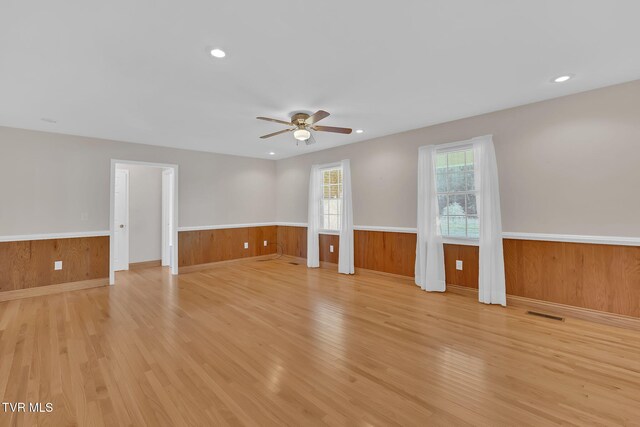 unfurnished living room with a wainscoted wall, ceiling fan, and light wood-style floors