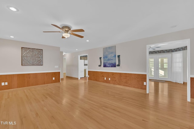 unfurnished living room with a ceiling fan, french doors, a wainscoted wall, and light wood finished floors