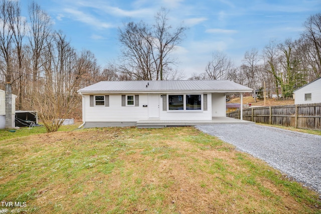 view of front of property with metal roof, gravel driveway, fence, and a front yard