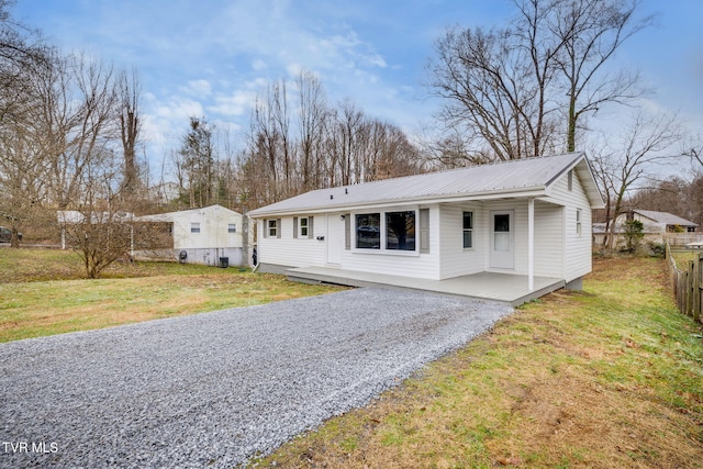 view of front of house with driveway, metal roof, fence, and a front lawn