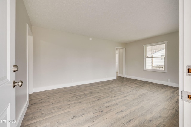 empty room featuring a textured ceiling, wood finished floors, and baseboards