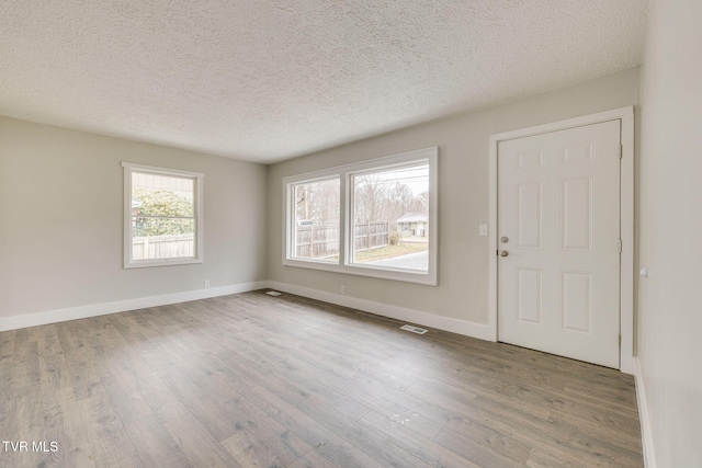 empty room featuring visible vents, a textured ceiling, baseboards, and wood finished floors