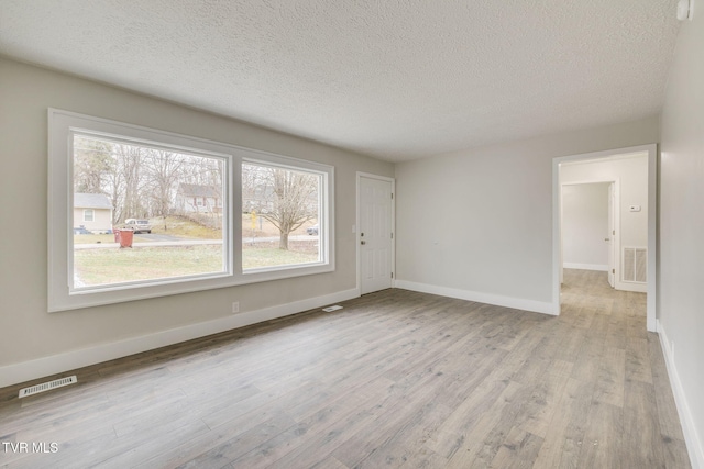 empty room featuring light wood-type flooring, baseboards, visible vents, and a textured ceiling