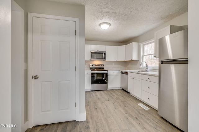 kitchen with stainless steel appliances, a sink, white cabinetry, light wood-style floors, and light countertops