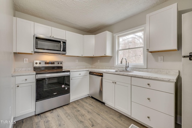 kitchen with stainless steel appliances, light wood finished floors, a sink, and white cabinets