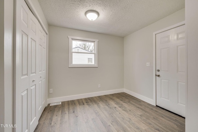 spare room featuring a textured ceiling, wood finished floors, visible vents, and baseboards