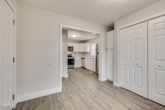 kitchen with a textured ceiling, white cabinetry, light countertops, appliances with stainless steel finishes, and light wood-type flooring