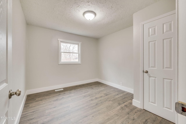 spare room featuring a textured ceiling, baseboards, and wood finished floors