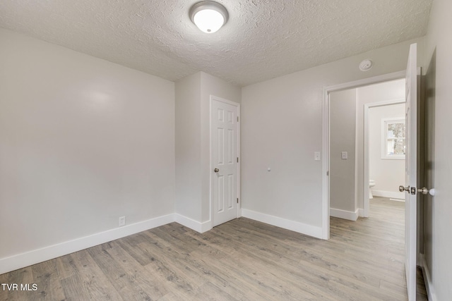 unfurnished room featuring a textured ceiling, light wood-type flooring, and baseboards