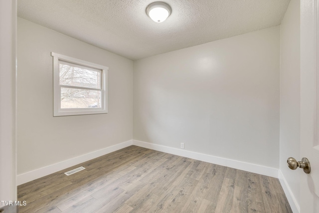 unfurnished room featuring baseboards, a textured ceiling, visible vents, and wood finished floors