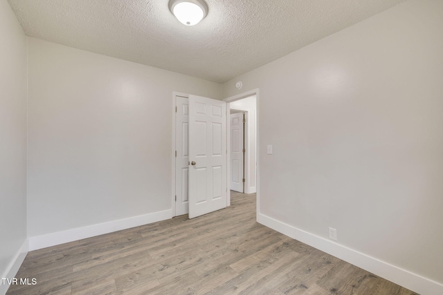 unfurnished room featuring light wood finished floors, baseboards, and a textured ceiling