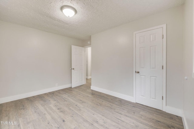 empty room with light wood-style flooring, baseboards, and a textured ceiling