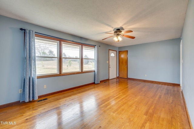 empty room featuring a textured ceiling, light wood-style flooring, visible vents, and baseboards