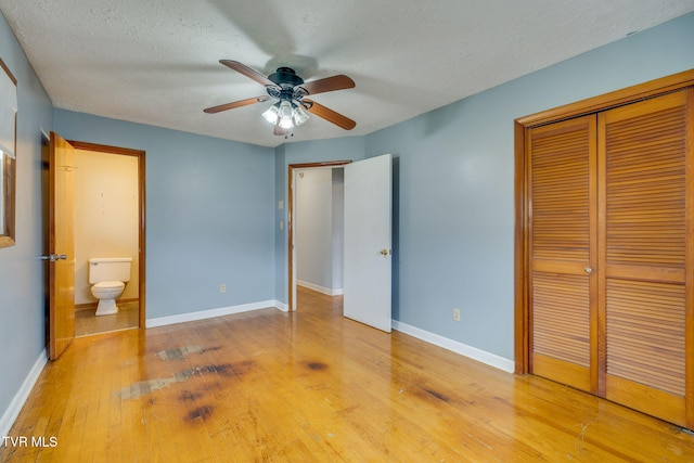 unfurnished bedroom featuring a closet, wood-type flooring, a textured ceiling, ensuite bath, and baseboards