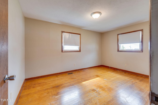 spare room with light wood-type flooring, visible vents, baseboards, and a textured ceiling