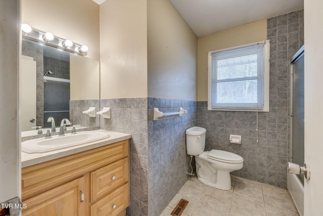 bathroom featuring visible vents, wainscoting, toilet, tile patterned floors, and tile walls