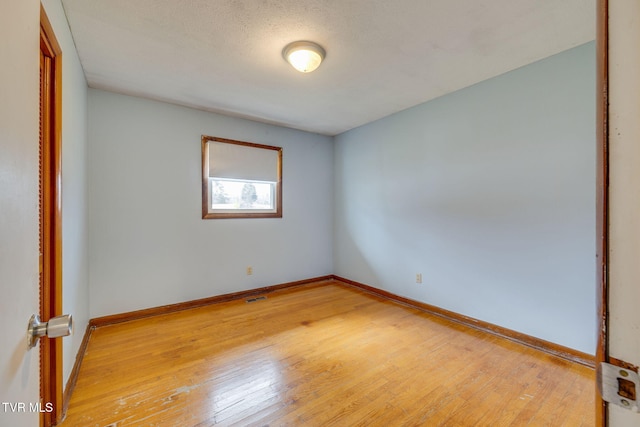 empty room with baseboards, visible vents, and light wood finished floors