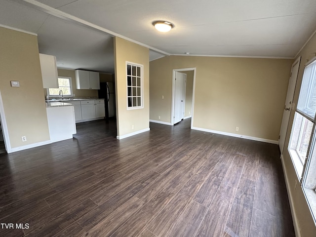 unfurnished living room with lofted ceiling, dark wood-type flooring, ornamental molding, a sink, and baseboards