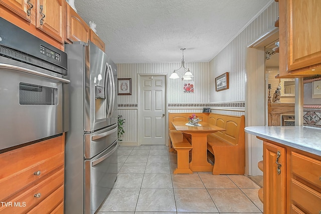 kitchen featuring a textured ceiling, a chandelier, appliances with stainless steel finishes, brown cabinetry, and wallpapered walls