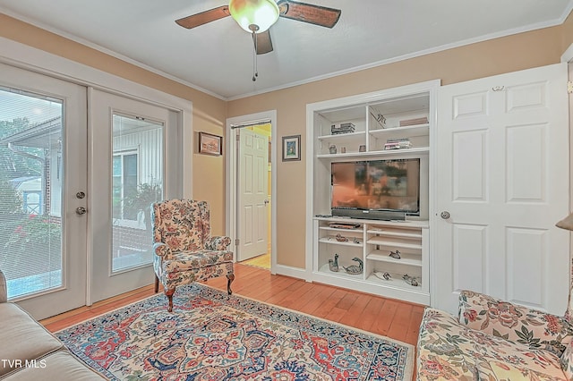 sitting room featuring light wood finished floors, built in features, ceiling fan, crown molding, and french doors