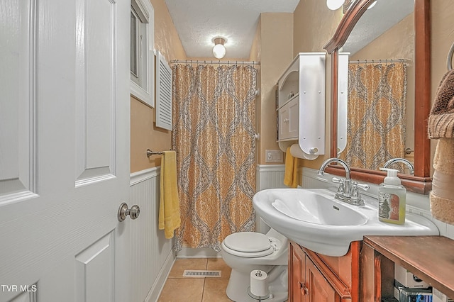 bathroom with visible vents, wainscoting, toilet, tile patterned floors, and a textured ceiling