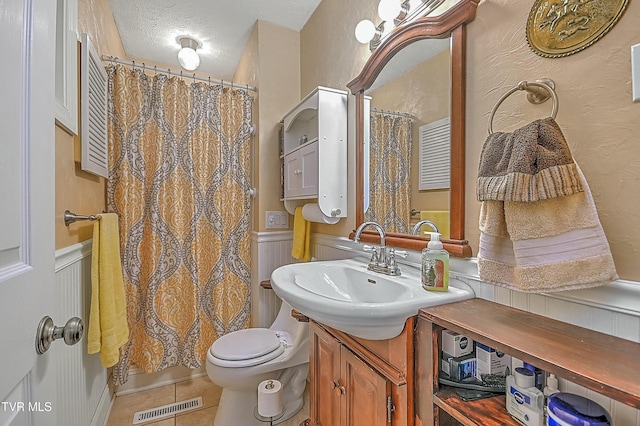 bathroom featuring a textured ceiling, tile patterned flooring, a wainscoted wall, vanity, and visible vents