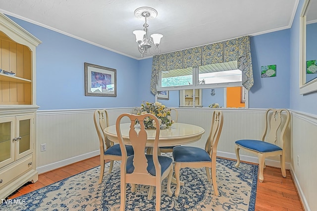 dining area featuring a wainscoted wall, ornamental molding, wood finished floors, and a notable chandelier