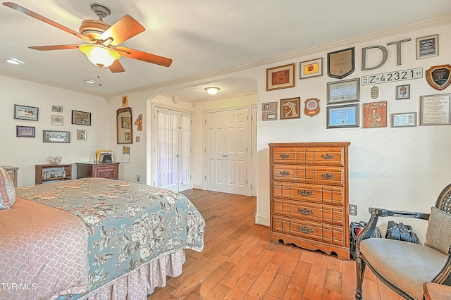 bedroom with arched walkways, a ceiling fan, ornamental molding, light wood-type flooring, and two closets